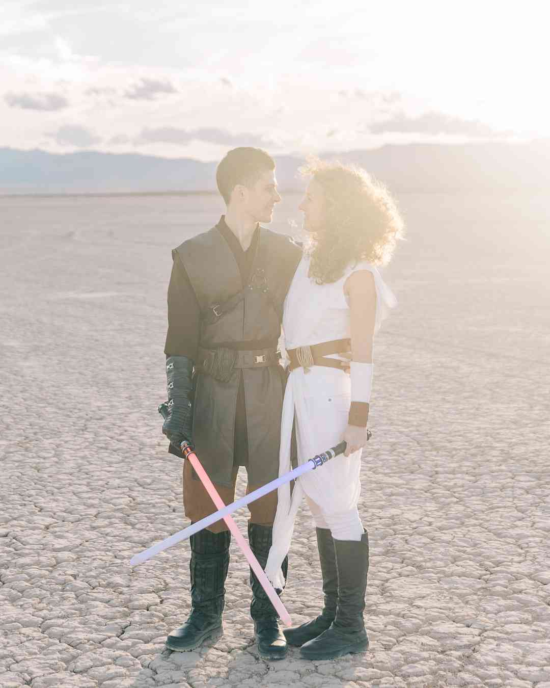 Couple déguisé en personnages de Star Wars, sabres laser en main, se regardant tendrement dans un désert.