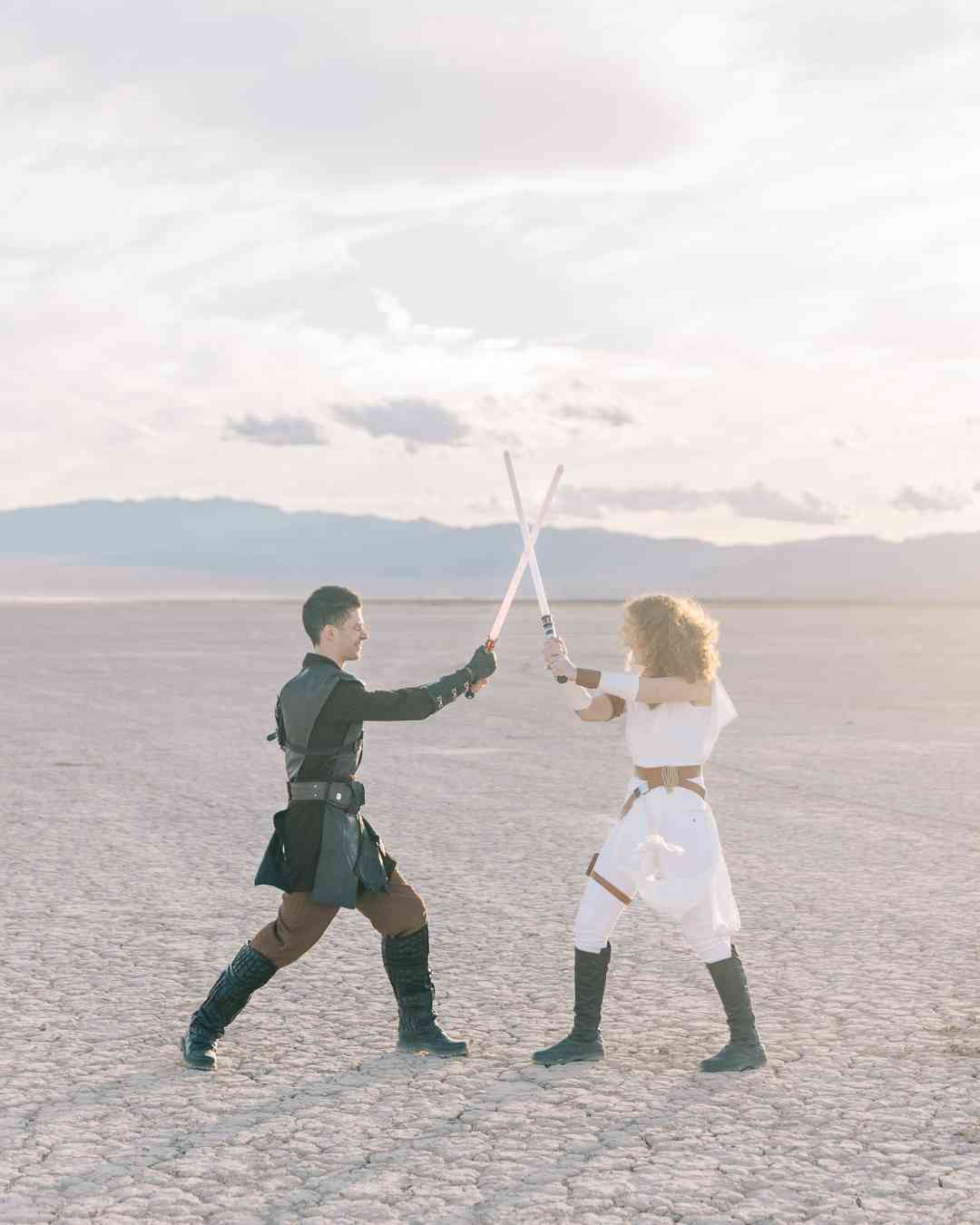 Couple déguisé en Jedi et Sith s’affrontant amicalement avec des sabres laser dans un paysage désertique.
