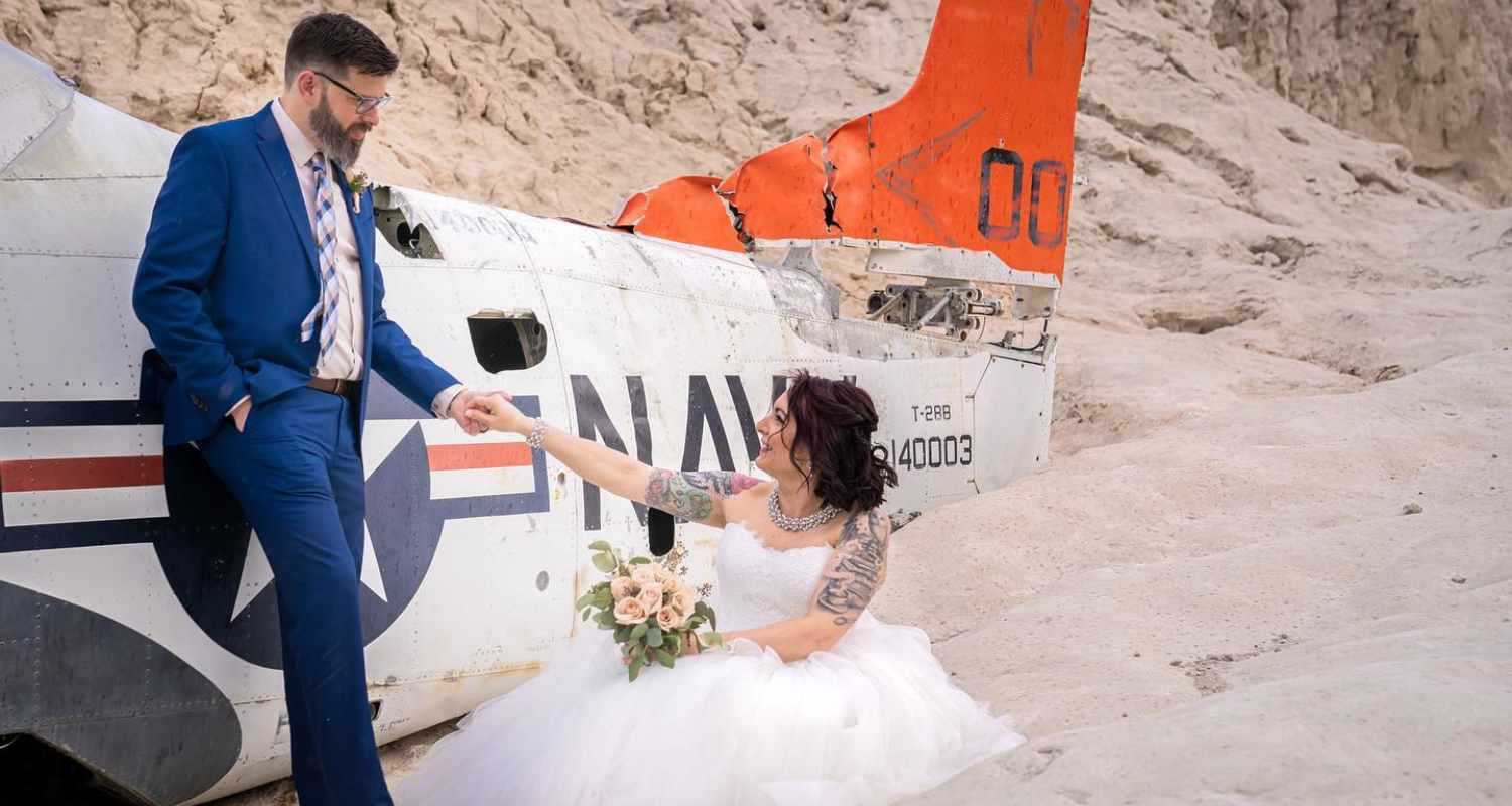 Couple de mariés posant devant une carcasse d’avion dans le désert