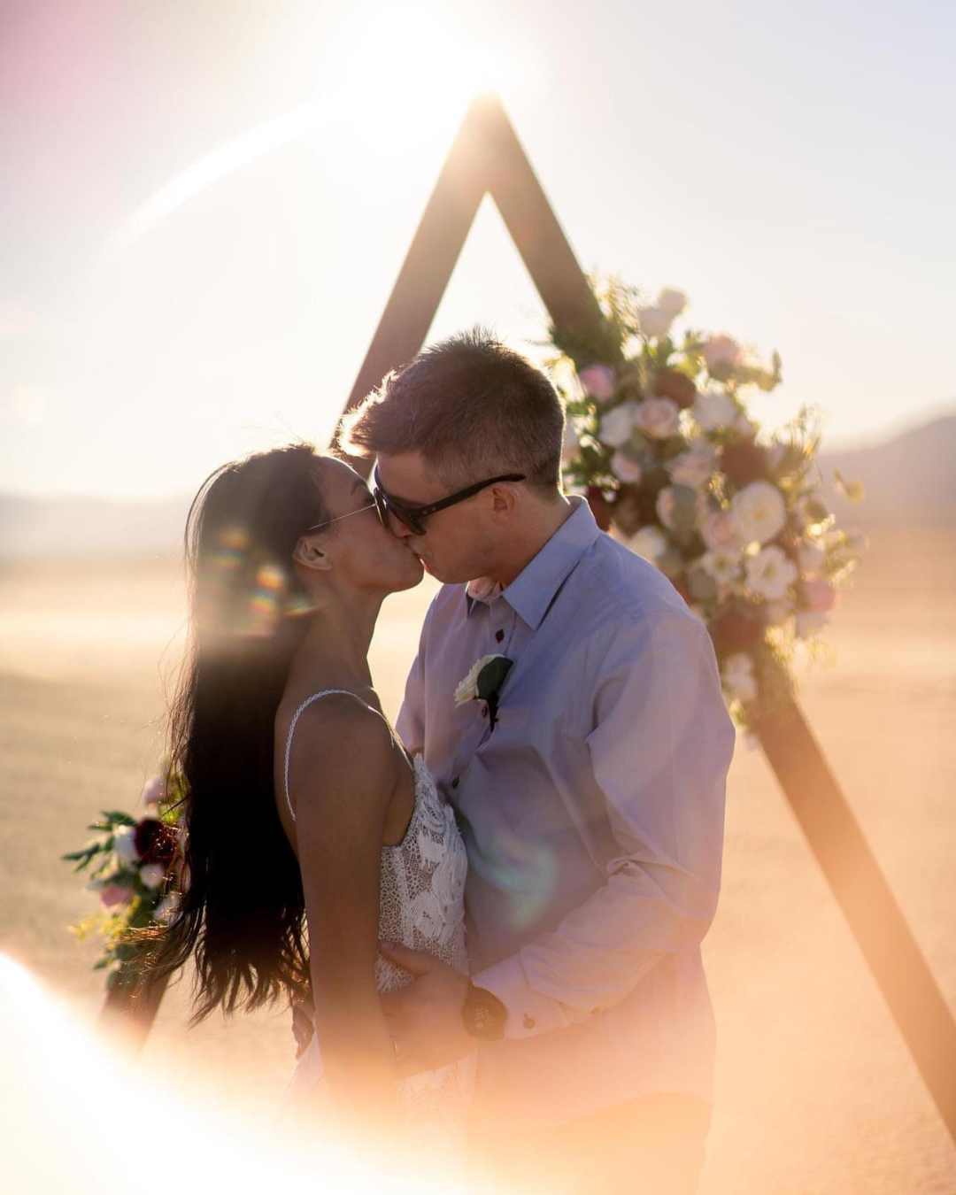 Couple s’embrassant devant une arche florale au coucher du soleil