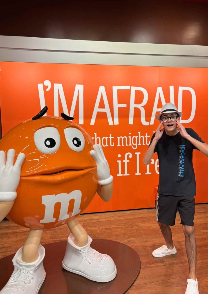 Photo avec la statue Orange M&M’s, Wyatt avec chapeau reprenant la mimique devant “I’M AFRAID”.