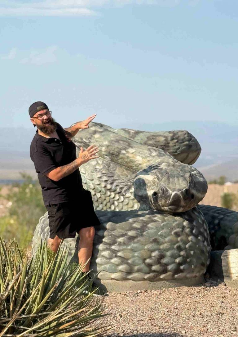 Une personne pose à côté d’un crotale géant sur un terrain de gravier.