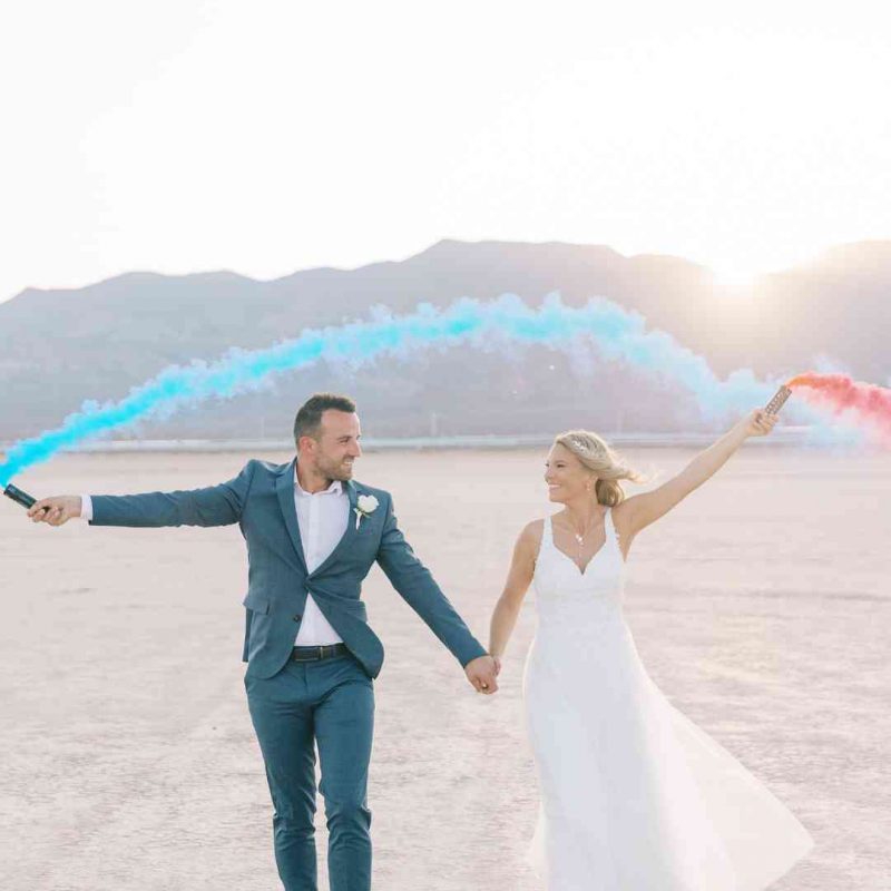 Couple en tenue de mariage tenant des fumigènes bleu et rouge au Dry Lake Bed près de Las Vegas – Crédit photo Pretty Day