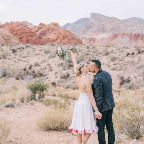 Couple de mariés s’embrassant dans le désert de Red Rock Canyon, bouquet levé en signe de célébration – Crédit photo Pretty Day