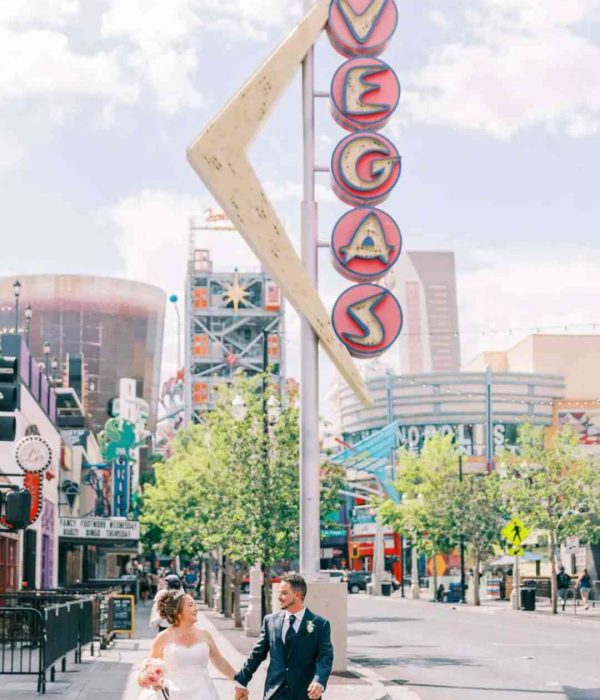 Couple de mariés marchant main dans la main sous le panneau vintage “VEGAS”.